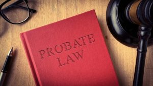 Probate law book on wooden table surrounded with gavel, glasses and pen.